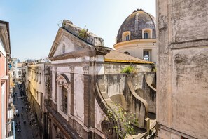 A narrow street flanked by historic buildings with classical architecture, including a dome and arched windows. - Tribunali Trendy Accommodations by Wonderful Italy (Naples)