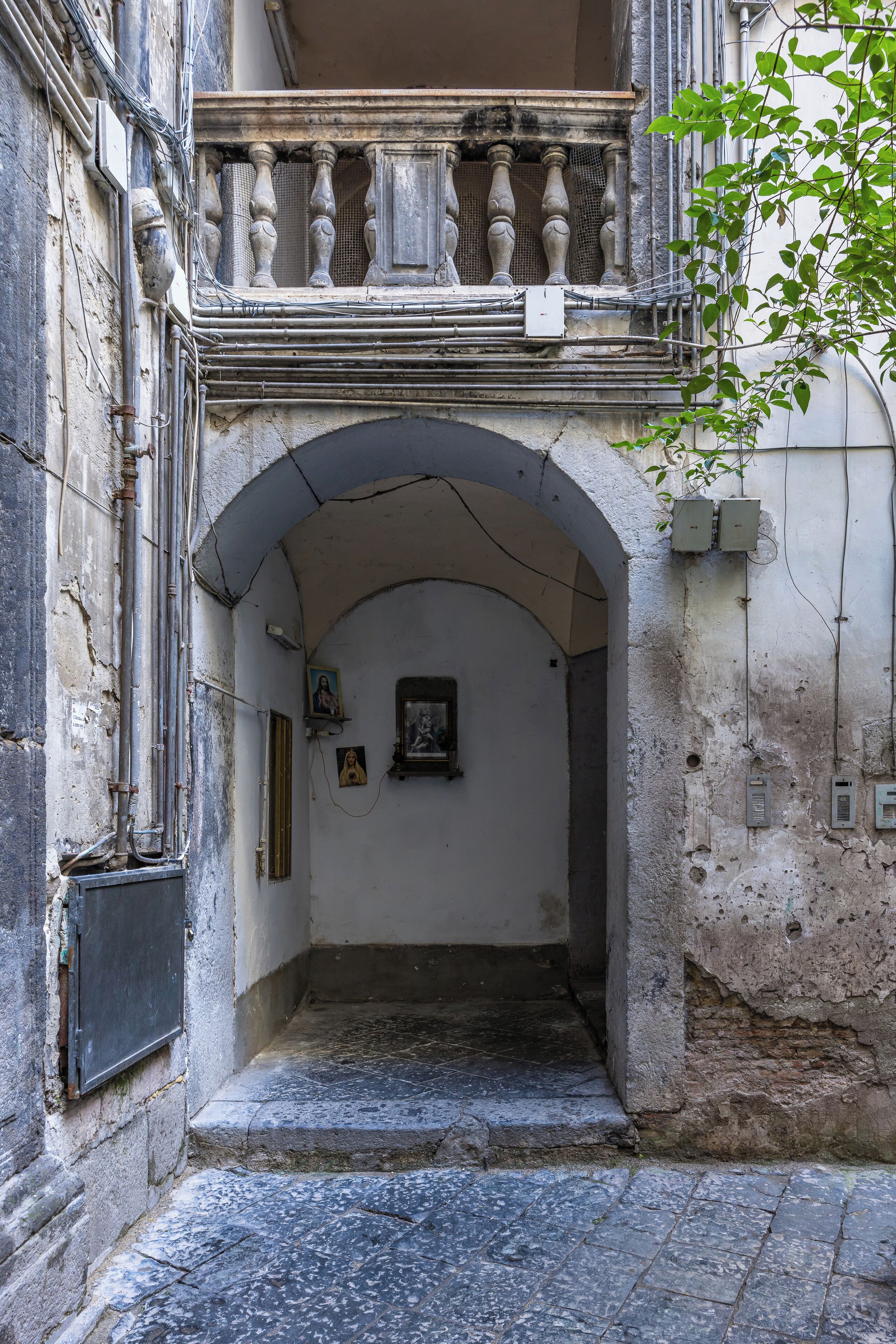 An arched doorway leading to a narrow passageway with a balcony above.