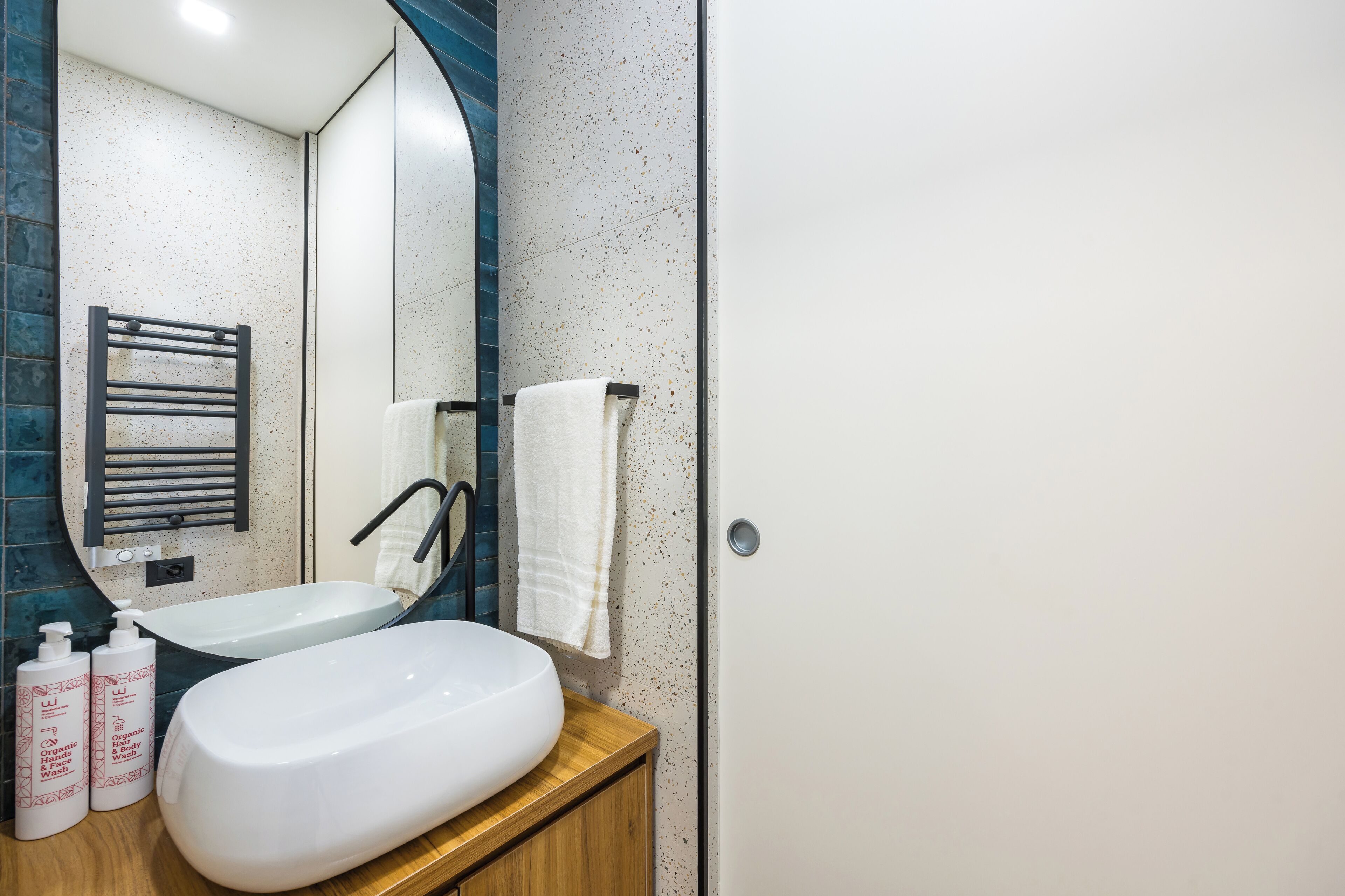A modern bathroom with a freestanding sink, a towel rack, and two bottles of organic body wash.
