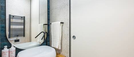 A modern bathroom with a freestanding sink, a towel rack, and two bottles of organic body wash.