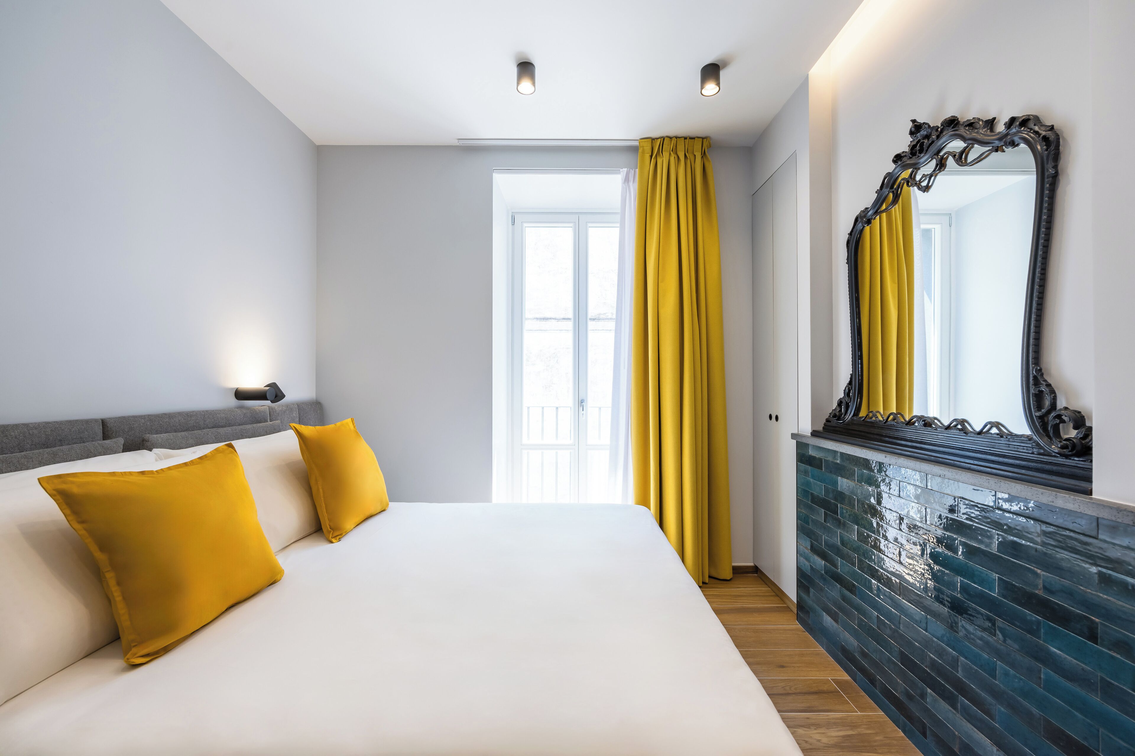 Een moderne hotelkamer met een groot bed, een spiegel en een raam met gele gordijnen.
