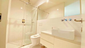 Un baño moderno con cabina de ducha de vidrio, lavabo blanco y retrete.