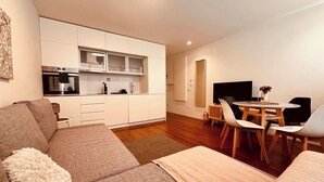 Una sala de estar moderna con un sofá, una mesa de comedor con sillas, y una zona de cocina con armarios y electrodomésticos.