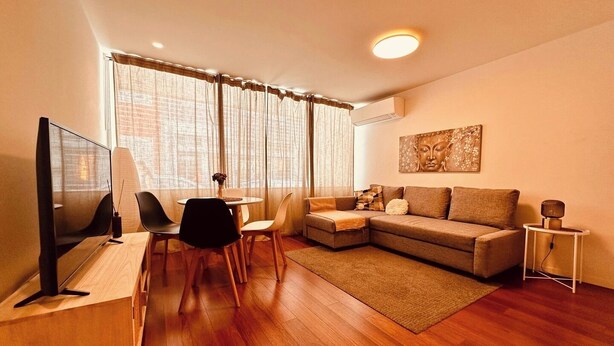 Una sala de estar moderna con televisor de pantalla plana, un sofá, una mesa de centro y un comedor con sillas.