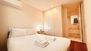 Habitación de hotel con cama, mesita de noche con lámpara, armario y baño visible a través de una puerta abierta.