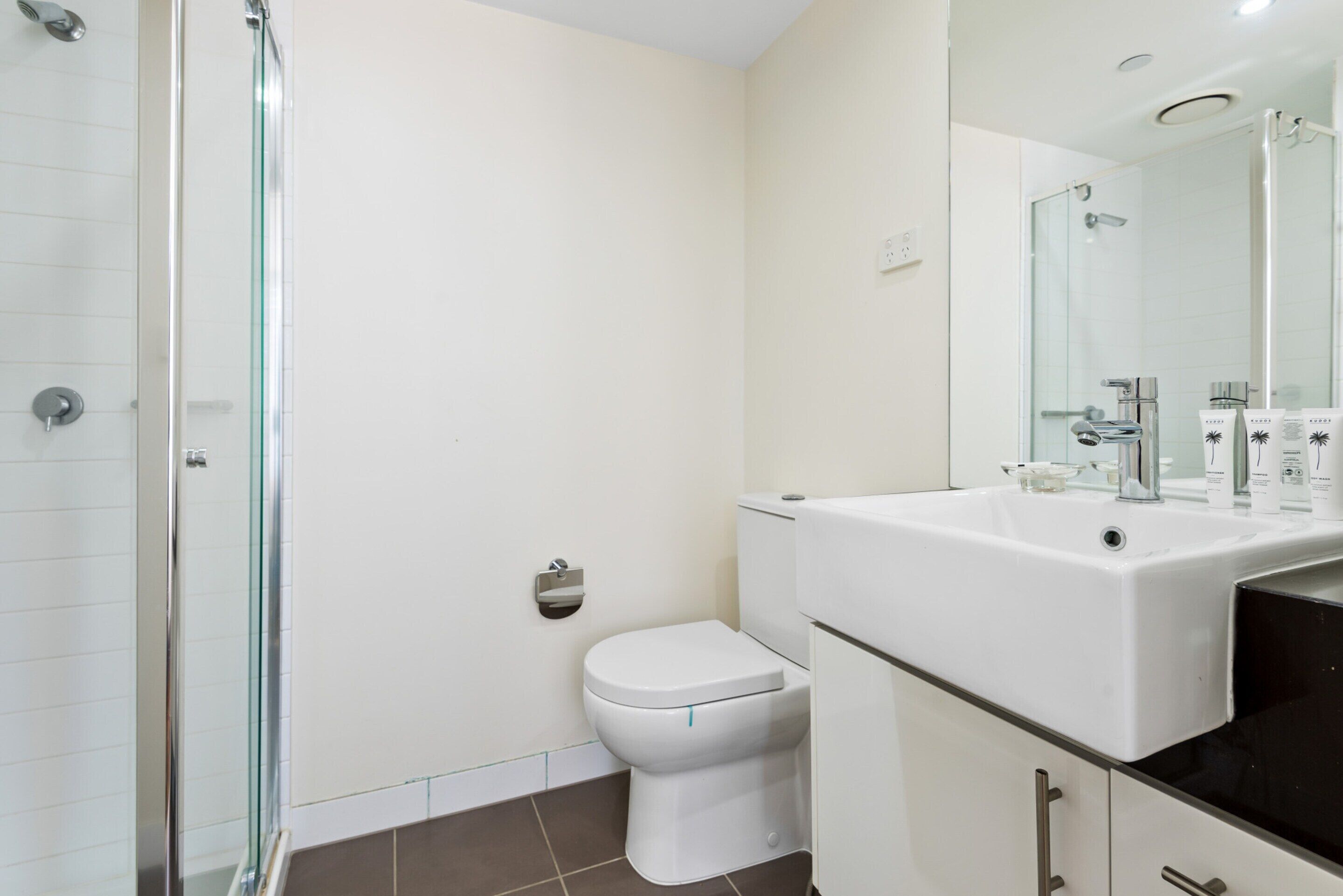 A modern bathroom with a glass shower enclosure, a white toilet, and a sink with a mirror above it.
