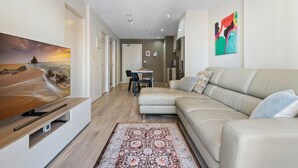 A modern living room with a beige sofa, a flat-screen TV, and a patterned rug. - Modern City Convenience With Great Amenities (Melbourne)
