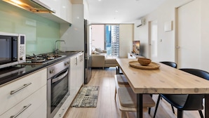 A modern kitchen with a gas stove, oven, and microwave. There is a dining area with a wooden table and chairs. - Modern City Convenience With Great Amenities (Melbourne)