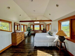 A bedroom with a large bed, wooden dresser, and a desk with a chair. There are multiple windows providing views of the outdoors. - Spacious Farmhouse Estate with Mountain Views & Dual Kitchens near Skiing and Trails in Tetonia, Idaho (Tetonia)