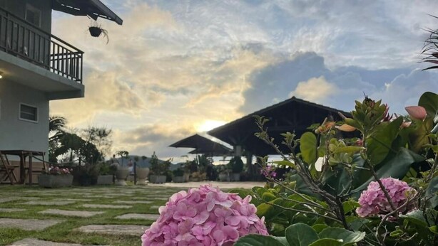 A garden with pink hydrangea flowers, a building with a balcony, and a cloudy sky. - Chácara da Sorte (Pacoti)