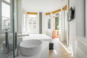 Een moderne slaapkamer met een groot wit bed, een ronde witte wastafel en een balkon met oranje leuningen.