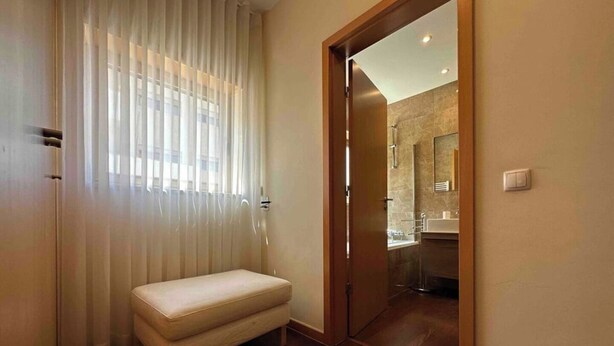 Une pièce avec un banc, une porte donnant sur une salle de bain et une fenêtre avec des rideaux.