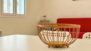 Una mesa de comedor blanca con un centro de mesa de madera, un sofá rojo y un cuadro de un atardecer sobre un puerto deportivo en la pared.