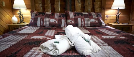 Una habitación tipo cabaña de madera con una cama, dos mesitas de noche y un cabecero con postes de madera tallada.