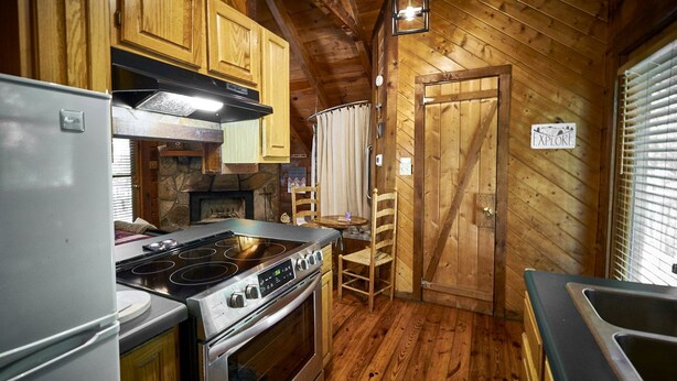 Une cuisine de taille réduite avec des murs en bois, une cuisinière, un réfrigérateur et un évier.