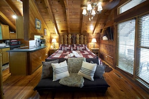 A log cabin interior with a wooden ceiling, a kitchenette, a bed with a quilt, and a window with blinds. - Stunning Wooden Cottage with Hot-tub in Sevierville, Tennessee (Sevierville)