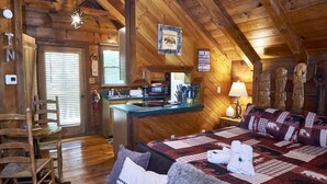 L’intérieur d’un chalet rustique, avec un plafond en bois, un lit confortable recouvert d’une courtepointe, un coin repas et une cuisine.