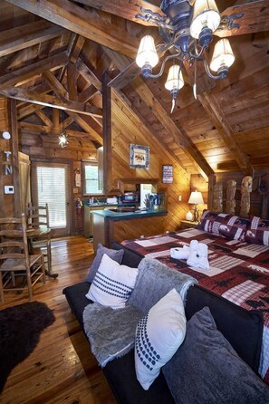 A rustic cabin interior with a wooden ceiling, a cozy bed with a quilt, a dining area, and a kitchen. - Stunning Wooden Cottage with Hot-tub in Sevierville, Tennessee (Sevierville)