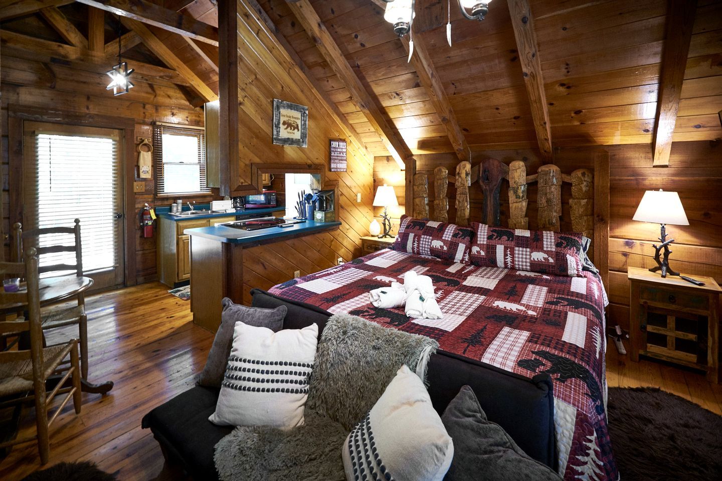L’intérieur d’une cabane en rondins, avec un plafond en bois, un lit recouvert d’une courtepointe, un bureau et une chaise.