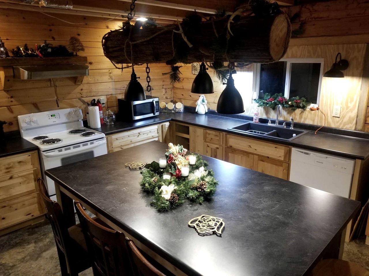 A kitchen with wooden cabinets, a central island, a stove, a microwave, and a sink.
