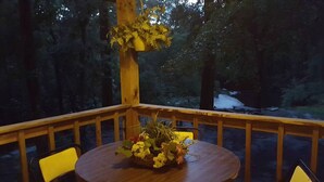 A wooden deck with a round table and two chairs, surrounded by a railing.