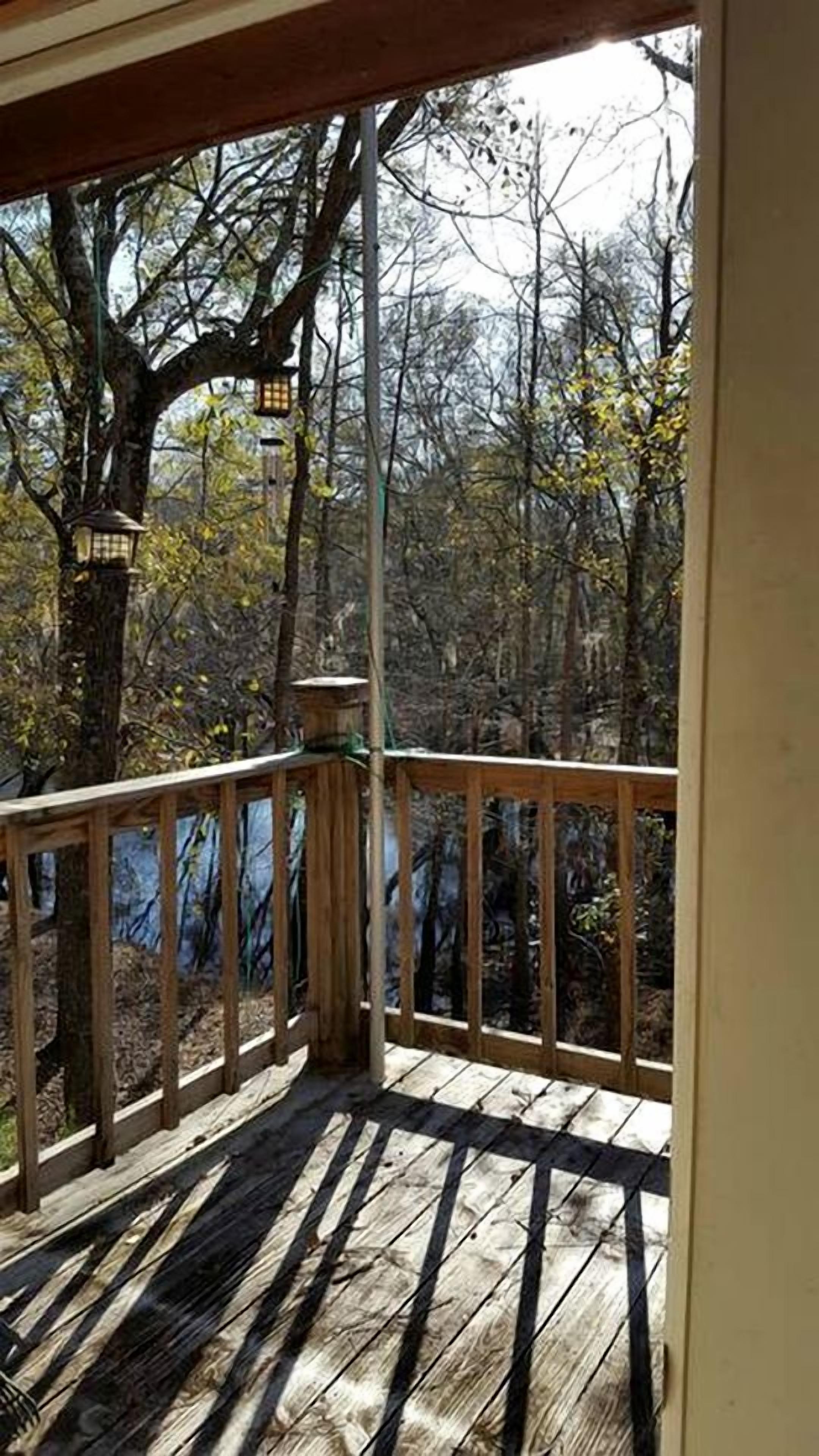 A wooden deck with a railing, a lantern, and a view of trees and foliage.