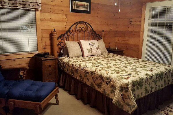 A wooden-paneled bedroom with a bed, nightstand, chair, and a picture on the wall.