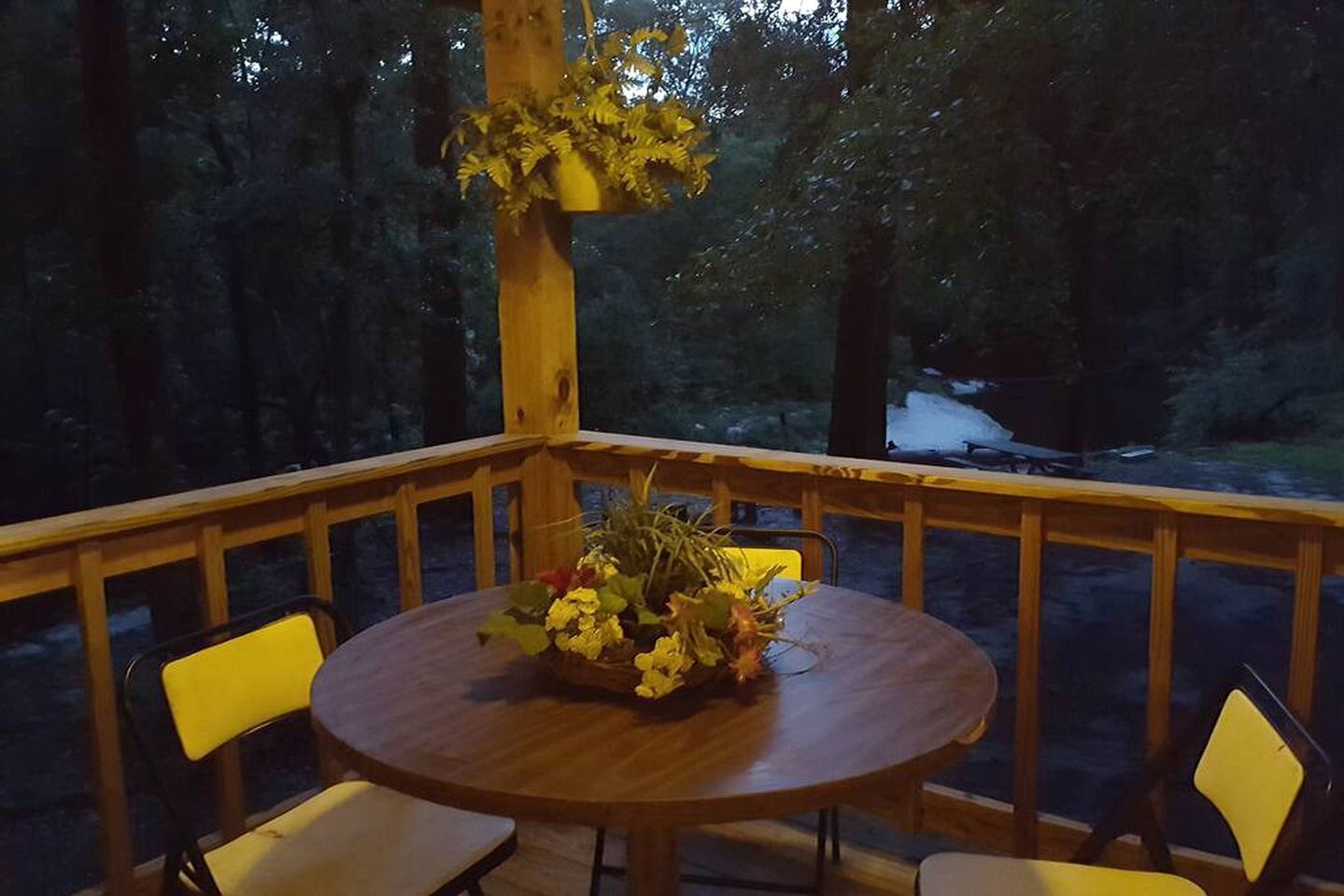Une terrasse en bois avec une table ronde et deux chaises, entourée d’une rambarde.