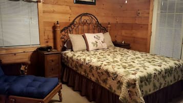 A wooden-paneled bedroom with a bed, nightstand, chair, and a picture on the wall.