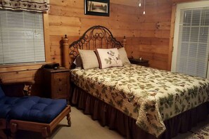 Un dormitorio con paneles de madera, una cama, mesita de noche, silla e imagen en la pared.