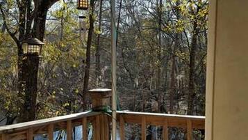 A wooden deck with a railing, a lantern, and a view of trees and foliage.