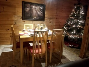 Un interior de madera con una mesa de comedor preparada para cuatro comensales, un árbol de Navidad y un cuadro en la pared.