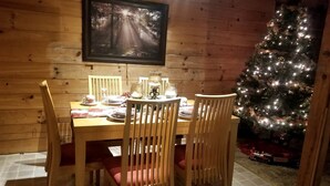 A wooden interior with a dining table set for four, a Christmas tree, and a framed picture on the wall.