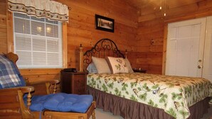A wooden cabin bedroom with a bed, a chair, a nightstand, and a window with blinds.
