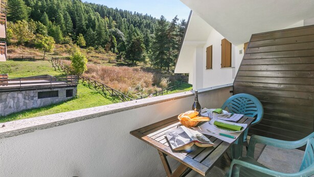 Un balcone con tavolo, sedie e vista su un pendio boscoso.