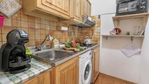 Una cucina compatta con mobili in legno, una lavatrice, una macchina da caffè e un forno a microonde.