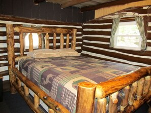 Ein gemütliches Schlafzimmer in einer rustikalen Holzhütte mit einem Bettgestell aus Holz, einer Steppdecke und einem Fenster mit karierten Vorhängen.