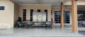 A covered outdoor area with a table and chairs, a ceiling fan, and a building entrance with windows and a door. - Capital O 91243 Bee Good Chalet (Kampung Kelewang Jatoh)