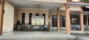 A covered outdoor area with a table and chairs, a ceiling fan, and a building entrance with a sign. - Capital O 91243 Bee Good Chalet (Kampung Kelewang Jatoh)