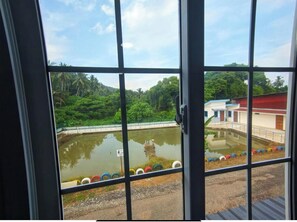 Vista a través de una ventana de metal, con una masa de agua y follaje al fondo.