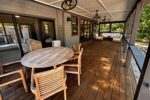 A covered outdoor patio with a wooden table and chairs, a sofa, and a ceiling fan. - Lakefront Cabin with Two Decks and Back Yard in Tennessee (Tracy City)