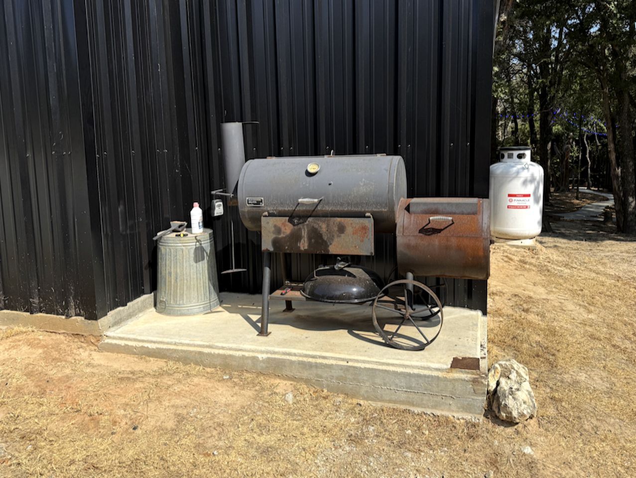 A portable grill with a gas tank and a propane cylinder, placed on a concrete platform.