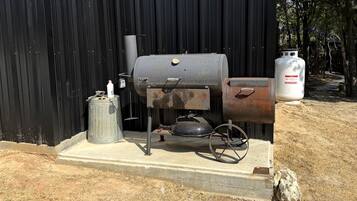 A portable grill with a gas tank and a propane cylinder, placed on a concrete platform.