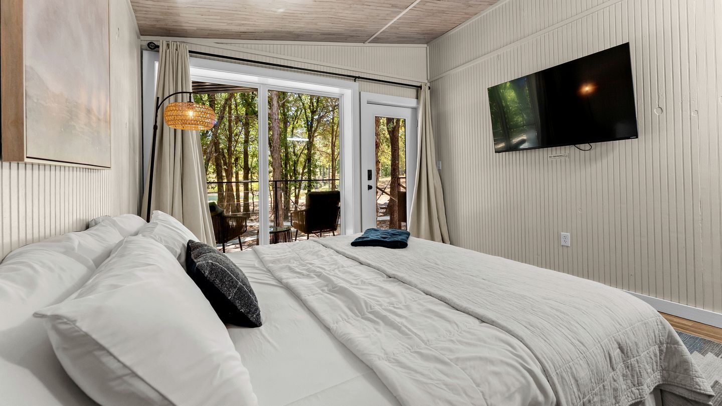 Un dormitorio con cama, televisor montado en la pared y vistas al exterior a través de un ventanal.