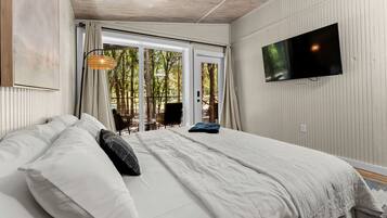 Un dormitorio con cama, televisor montado en la pared y vistas al exterior a través de un ventanal.