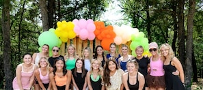 Un groupe de personnes se tient devant une structure en bois, décorée de ballons de couleurs vives.