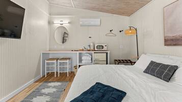 Un dormitorio con cama, escritorio con silla, lámpara colgante y aire acondicionado instalado en la pared.