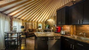 A cozy interior with a wooden ceiling, a dining area with a round table and chairs, a kitchen with dark cabinets and a red appliance, and a wooden wall. - Stunning Yurt with Magnificent Creek Views in Topton, North Carolina (Topton)