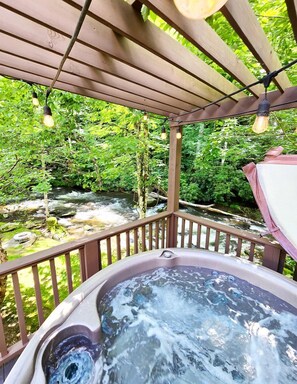 A hot tub on a wooden deck with a view of a flowing river and greenery. - Stunning Yurt with Magnificent Creek Views in Topton, North Carolina (Topton)