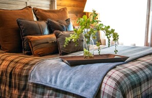 A bed with plaid bedding, leather pillows, and a glass vase with green plants. - Stunning Yurt with Magnificent Creek Views in Topton, North Carolina (Topton)